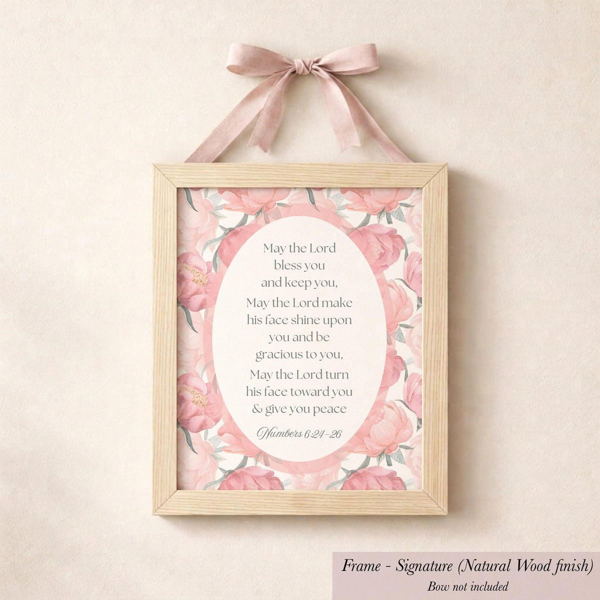 A framed sign with a pink floral design hangs on a wall, featuring a religious text.