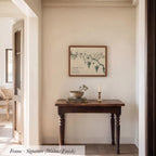 a wooden table with a bowl and a candle on it, set against a white wall with a framed picture hanging above it.