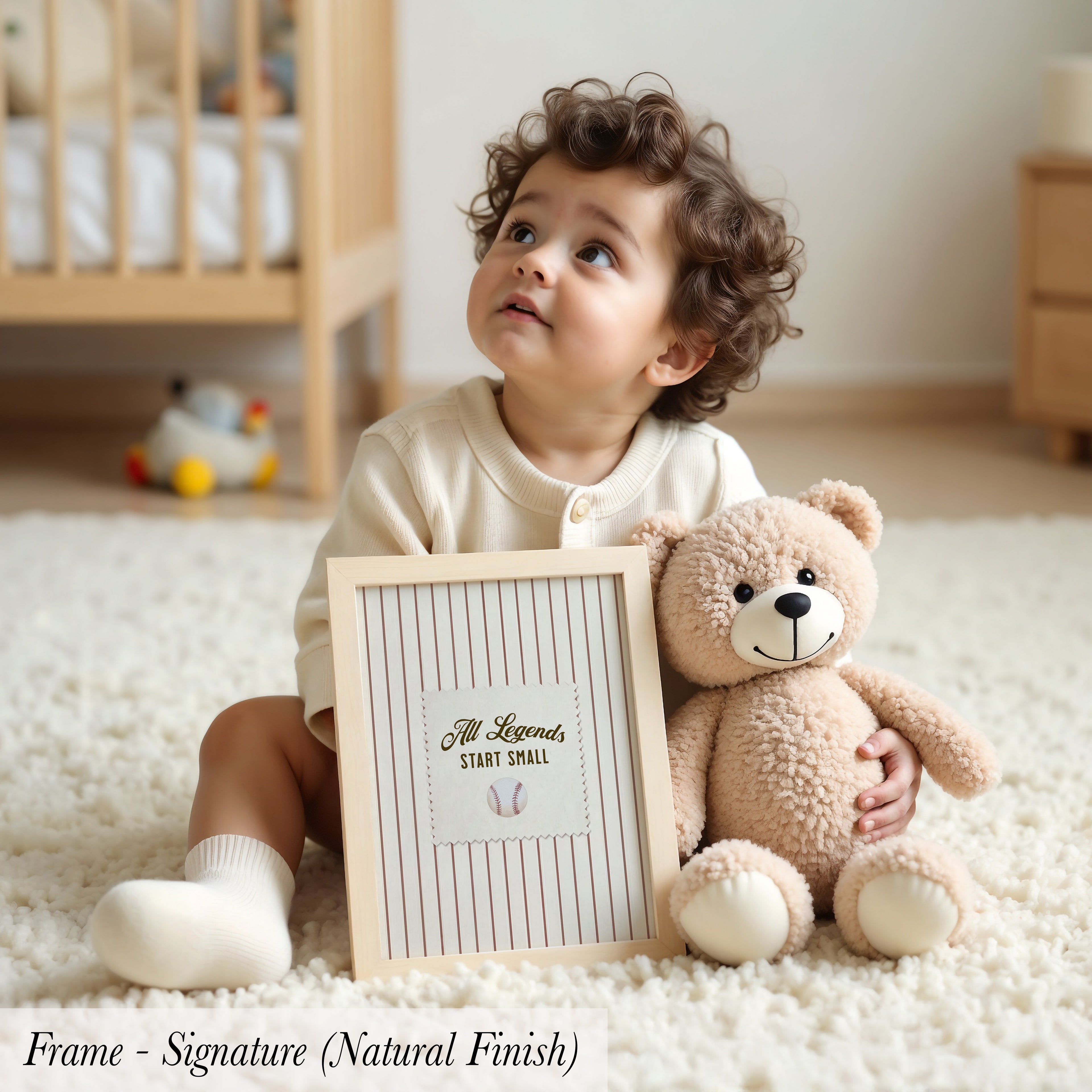 A young child sits on the floor, holding a picture frame with the text "All Legends Start Small" inside it, accompanied by a teddy bear.