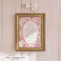 A framed print with a pink floral design hangs on a wooden wall.