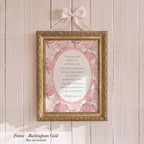A framed print with a pink floral design hangs on a wooden wall.