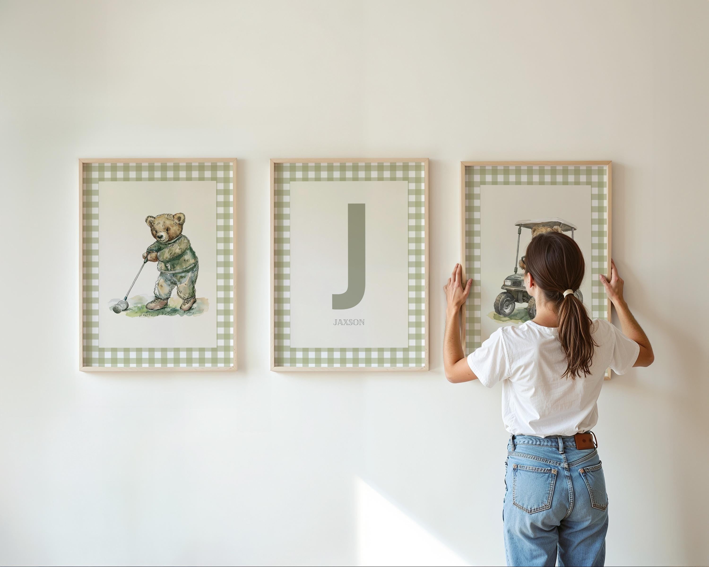 A woman is hanging three framed pictures on a wall.
