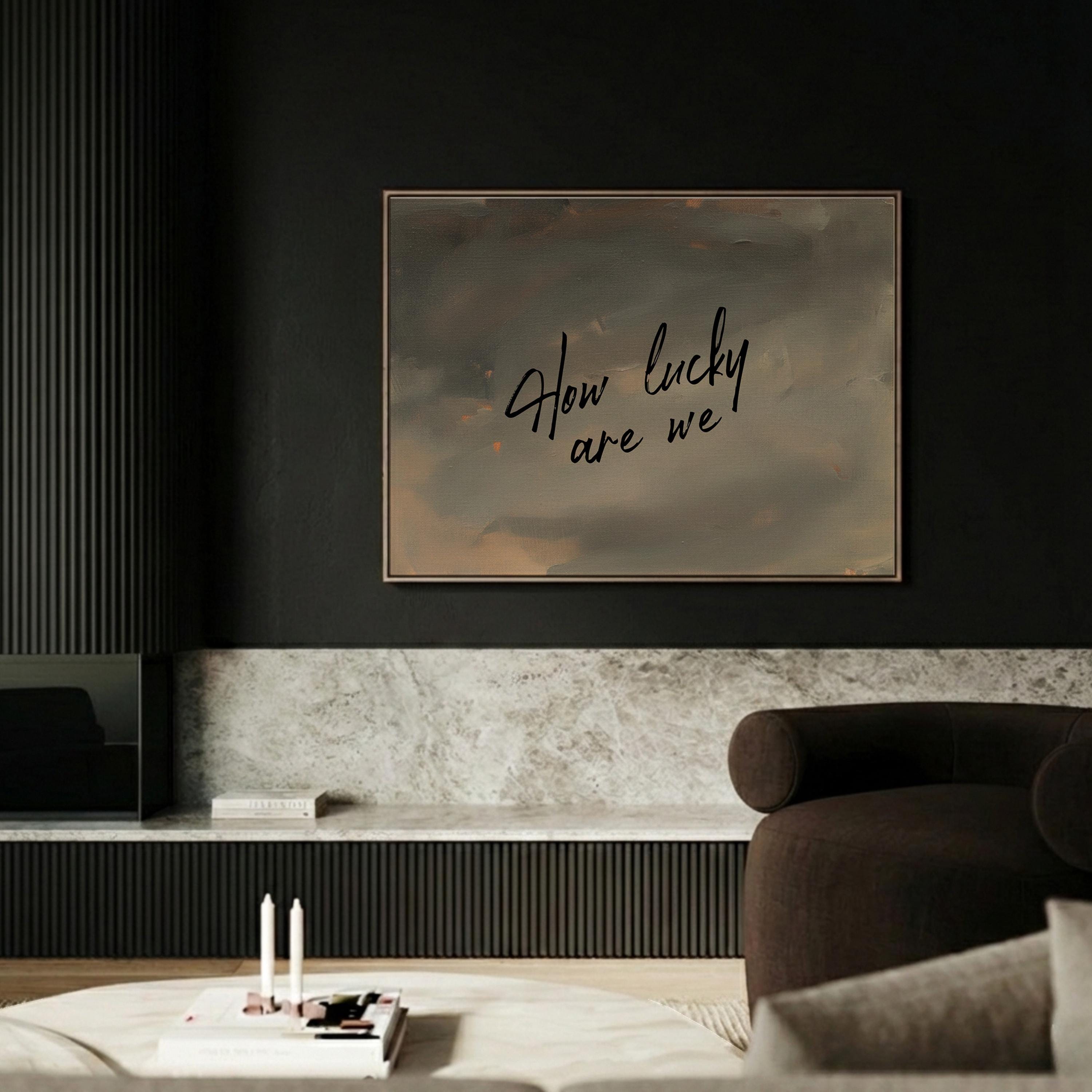 a modern living room with a dark color scheme and a large framed text on the wall that reads "How lucky are we".
