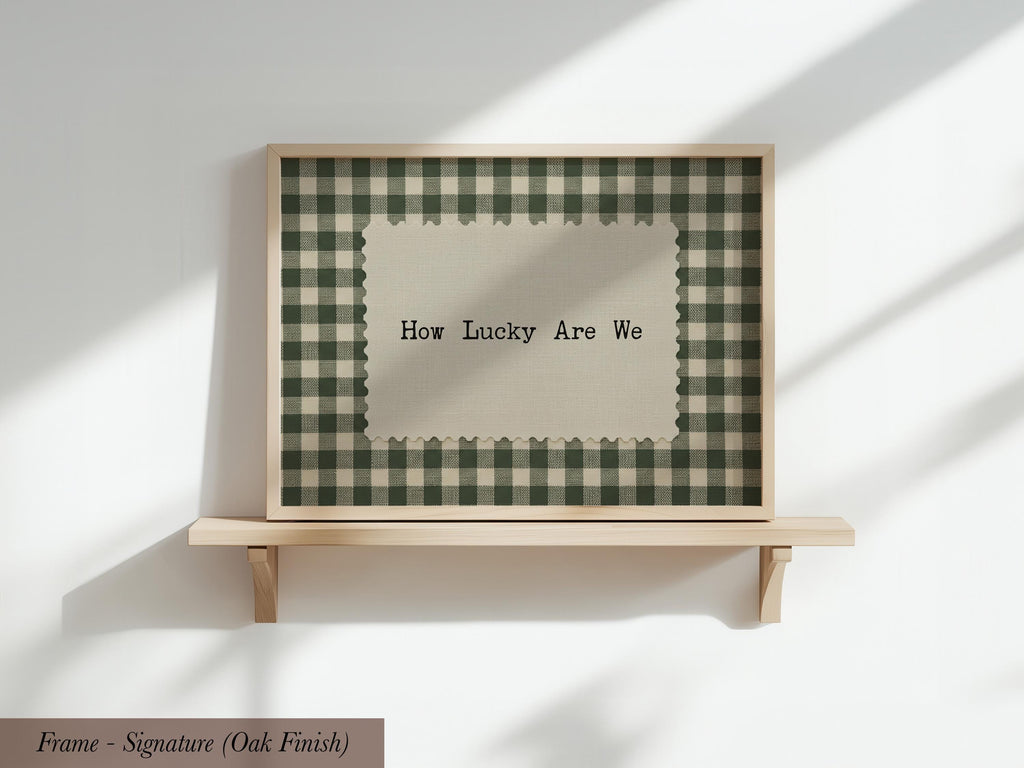 A framed picture with a checkered pattern and the text "How Lucky Are We" displayed on it, mounted on a wooden shelf against a white wall.