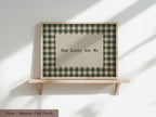 A framed picture with a checkered pattern and the text "How Lucky Are We" displayed on it, mounted on a wooden shelf against a white wall.