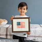 A young boy is holding up a framed picture of an American flag, smiling at the camera.