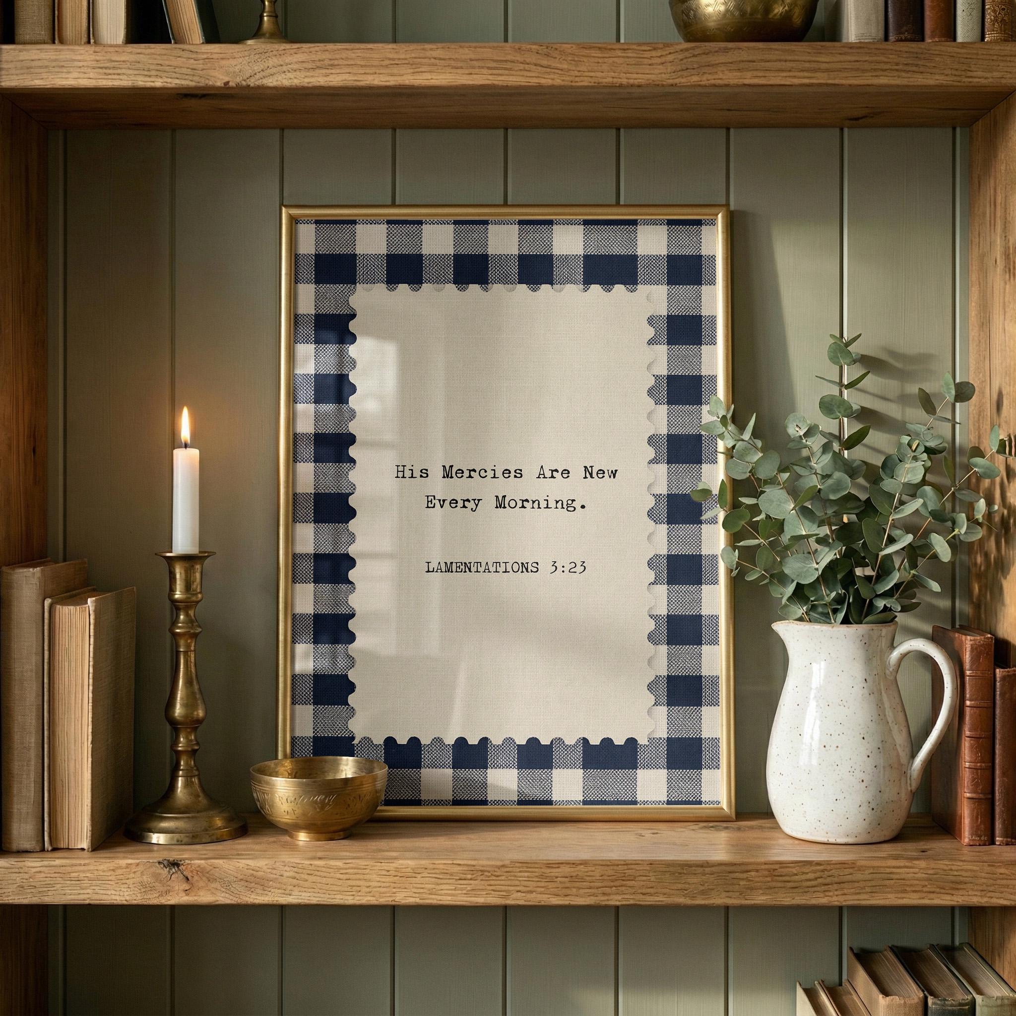 a framed Bible verse with a blue and white checkered border, placed on a wooden shelf next to a white vase with greenery and a lit candle.
