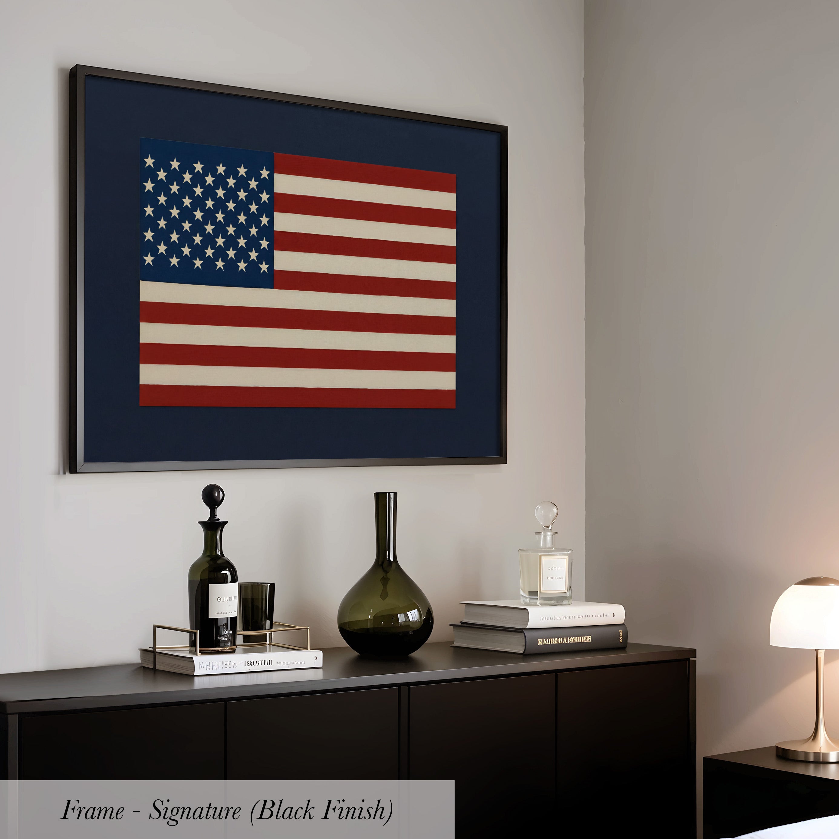 a framed American flag hanging on a wall above a black dresser with various decorative items on top, including a bottle, a vase, and a stack of books.