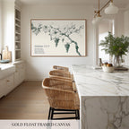 a modern kitchen with a large framed canvas of grapes hanging on the wall above a marble countertop. The kitchen has white cabinets and a marble countertop, and there are wicker chairs and a bowl of fruit on the counter.
