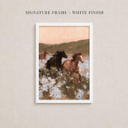 The image is a framed painting depicting three horses running through a field of flowers.