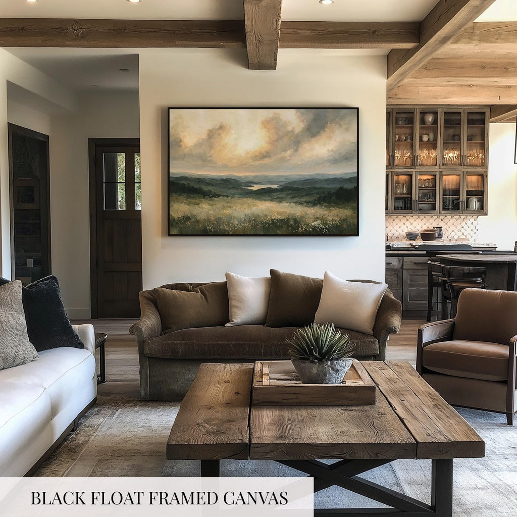a living room with a large black-framed canvas painting hanging on the wall, depicting a scenic landscape. The room is furnished with a couch, a chair, and a coffee table, creating a cozy and inviting atmosphere.